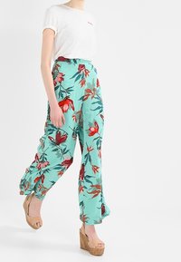 Spodnie w kwiatowy wzór w miętowym kolorze, o luźnym kroju i ściągaczach, zestawione z białą koszulą na krótki rękaw i beżowymi platformami.