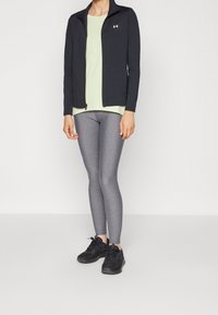 Svart zip-up idrottsjacka, ljusgrön mesh-topp och grå tights. Svarta träningsskor fulländar outfiten. Slät textur, åtsittande design.