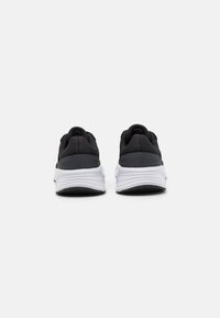 Chaussures de sport noires avec une tige en tissu texturé, des détails gris contrastants et une semelle intermédiaire blanche. Talon arrondi et semelle en caoutchouc.