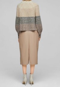 Maglione lavorato a maglia con texture a coste, caratterizzato da strisce beige, verdi e marroni. Abbinato a una gonna beige in ecopelle e stivaletti chiari alla caviglia.