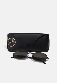 Ray-Ban prillid matist mustas metallraamis tumedate läätsede ja tekstureeritud musta nahkkattega, mis on kaunistatud kuldse logoga.