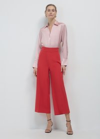 Camicia di raso rosa chiaro con colletto, abbinata a pantaloni a gamba larga rossi con vita alta. Sandali neri con tacco completano l'outfit.
