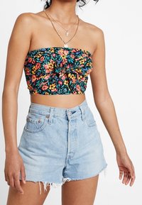 Femme portant un crop top floral sans bretelles avec un nœud à l'avant et un short en denim bleu clair taille haute avec des bords effilochés.