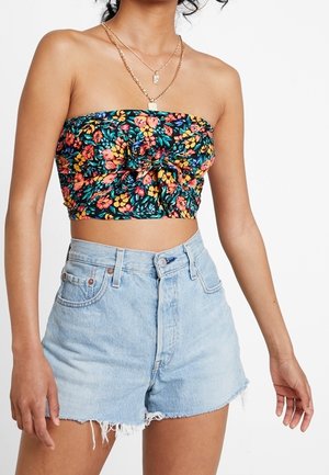 Femme portant un crop top floral sans bretelles avec un nœud à l'avant et un short en denim bleu clair taille haute avec des bords effilochés.
