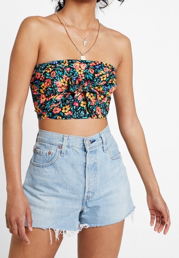 Femme portant un crop top floral sans bretelles avec un nœud à l'avant et un short en denim bleu clair taille haute avec des bords effilochés.