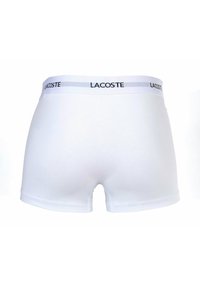 Boxer da uomo bianchi realizzati in un tessuto morbido con un design aderente. Presentano un cinturino elastico a contrasto con il marchio "Lacoste".