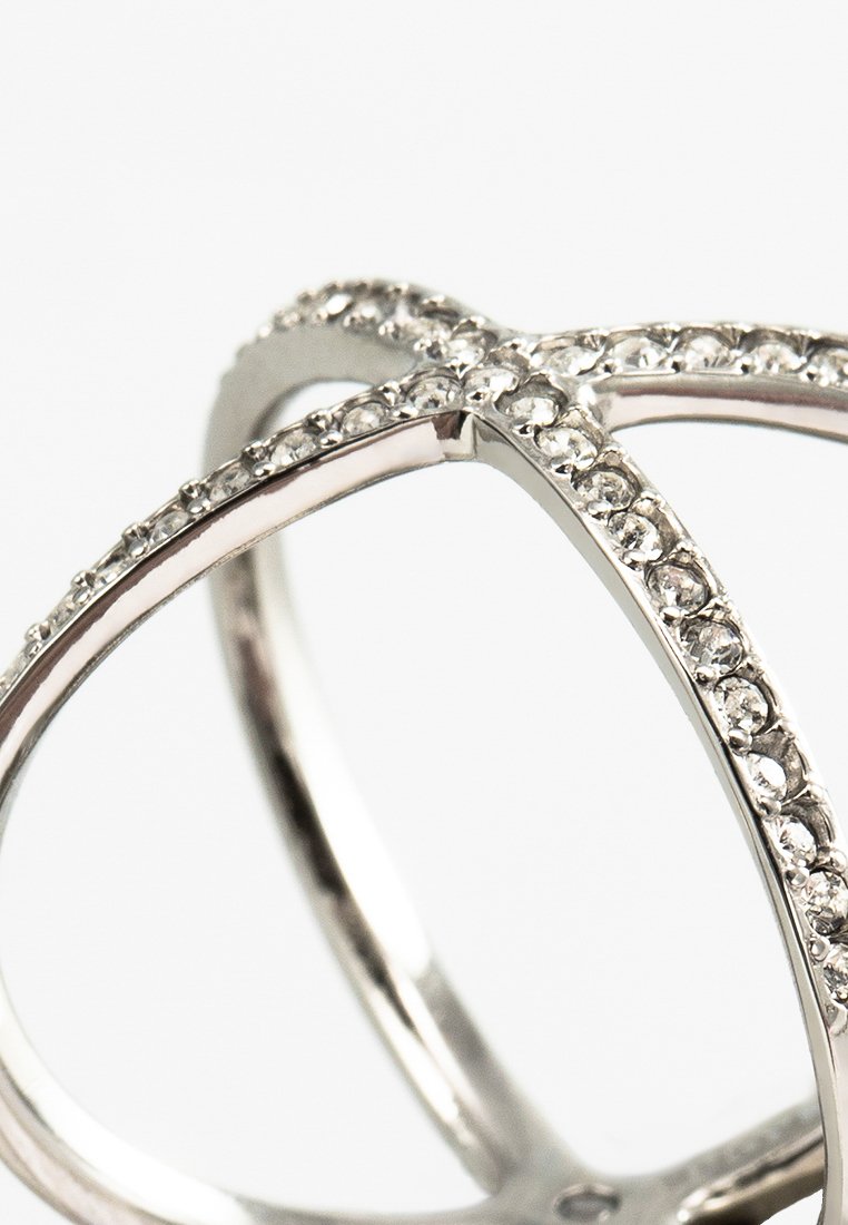 Anillo cruzado plateado con bandas intrincadas engastadas con cristales transparentes, que destaca por su textura suave y su acabado reflectante.