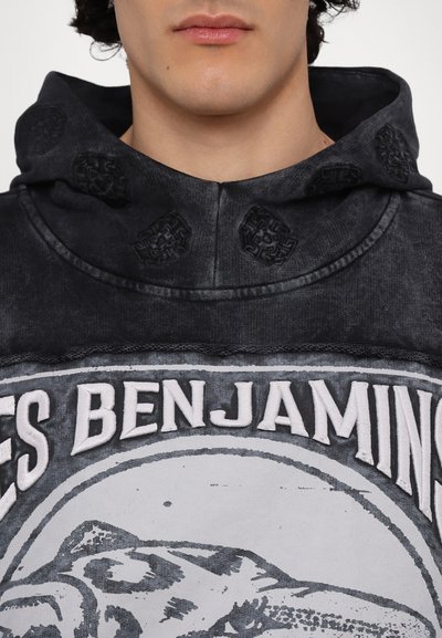 Hoodie noir avec des accents brodés, présentant un design graphique sur le devant et des détails texturés sur la capuche, fabriqué à partir d'un tissu doux.