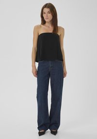 Schwarzes trägerloses Oberteil mit lockerem Schnitt, kombiniert mit hochsitztenden, weiten blauen Jeans aus Denim. Der Stoff wirkt glatt und ohne sichtbare Muster.