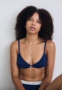 Soutien-gorge marine à fines bretelles, avec un petit accent logo rouge et blanc. Texture en tissu douce. Assorti avec un slip marine.