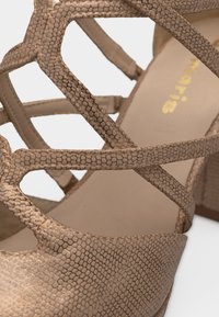 Μπεζ σανδάλι με λουριά, με επάνω μέρος από συνθετικό υλικό με υφή και εξαγωνικό μοτίβο, και χαμηλό τακούνι τύπου block.