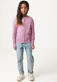 Rosa stickad kofta med strukturerat mönster, rund halsringning och knappar, parat med ljusblå jeans och vita sneakers.