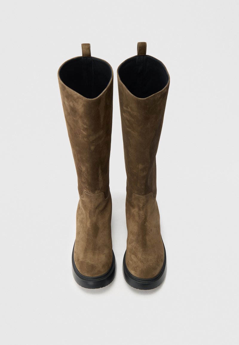 Stivali beige scamosciati al ginocchio con texture liscia, punta arrotondata e suola in gomma nera. Include un anello posteriore per facilitare la calzata.