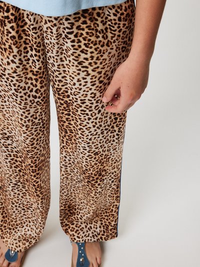 Pantalones de pierna ancha con estampado de leopardo, hechos de tela suave, que presentan tonos de beige y marrón, con un diseño fluidos y un detalle acentuado lateral.