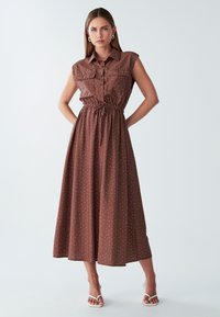 Brown, sleeveless maxi dress with a button-up front, elastic waist, and white polka dots. Smooth fabric with a relaxed fit.
