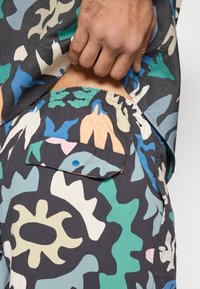 Βαμβακερό πουκάμισο σε σκούρο γκρι με έντονο, αφηρημένο σχέδιο καμουφλάζ σε πράσινο, τιρκουάζ, ροδάκινο και κρεμ. Διαθέτει ελαστική μέση.