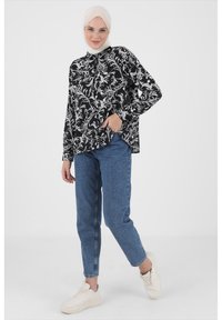 Black and white floral patterned blouse with a collar, paired with light blue tapered jeans and cream sneakers. Smooth fabric, relaxed fit.