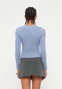 Jasnoniebieska bluzka z długim rękawem o dopasowanym kroju, w komplecie z szarą mini spódnicą z warstwowym wykończeniem. Gładki materiał, prosty okrągły dekolt.