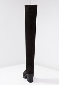 Botas negras de ante por encima de la rodilla, con un tacón grueso, textura suave y un diseño ajustado sin herrajes visibles.