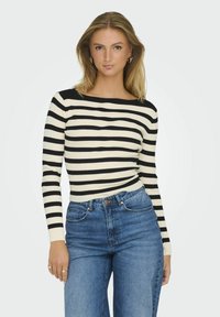 Svart och krämrandig ribbad långärmad topp med vid halsringning, kombinerad med högmidjade blå jeans. Tyget visar ett texturerat mönster.