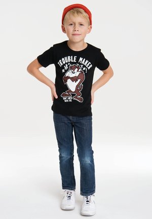 Black cotton t-shirt featuring a cartoon character with the text "TROUBLE MAKER" in white. Worn with blue jeans and white sneakers. Red beanie.