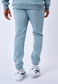 Pantaloni della tuta azzurri chiari realizzati in materiale morbido, con polsini a costine, vestibilità comoda e tasche laterali, abbinati a sneaker bianche.
