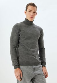 Grå polotröja gjord av ett mjukt stickat material, med en figurnära design, långa ärmar och ribbade muddlinningar, i kombination med ljusgrå jeans.