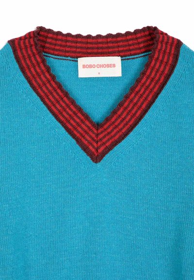 Pull en maille bleu avec un col en V côtelé rayé rouge et rouge foncé et une étiquette blanche portant la mention Bobo Choses.