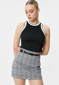 Schwarzes, geripptes Tanktop mit weißem Saum, kombiniert mit einem grauen, karierten Minirock und einem schwarzen Gürtel. Hauteng mit einer strukturierten Oberfläche.