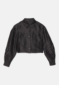Chemise noire courte à manches longues boutonnée, col pointu, deux poches poitrine et motifs découpés décoratifs avec clous sur les manches.