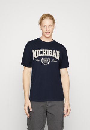 Camiseta azul marino de algodón con mangas cortas, con la inscripción "MICHIGAN" en texto crema y un logotipo circular con "1988". Diseño simple.