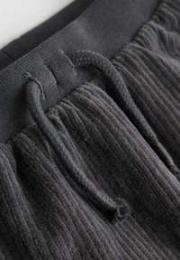 Tumehall ribaline kangas, millel on reguleeritav nöörivöö. Tekstuuri pehme ja sametine, põhjas on kootud nöör kohandamiseks.