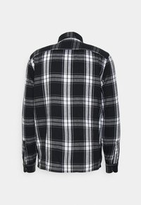 Svart och vit rutig skjorta med långa ärmar, knäppningar vid ärmsluten och krage. Har ett lätt tyg med en mjuk struktur och ett enhetligt mönster.