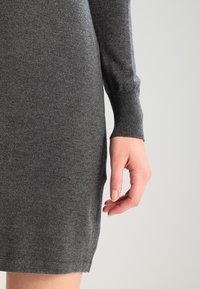 Harmaa neulemekko pitkillä hihoilla, jossa on ribbikuviointi hihansuissa ja muotoiltu siluetti, päättyen juuri polven ylle.