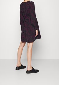 Czarna sukienka z różowymi falistymi wzorami, z długimi rękawami, luźnym krojem i wiązaniem w pasie. Czarne buty wsuwane z masywną podeszwą.