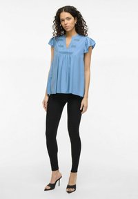 Blue, short-sleeve tunic top with a V-neck and textured detailing; paired with black skinny pants and heeled mules.
