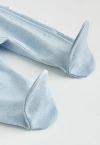 Moufles en tissu doux bleu clair avec compartiments pour le pouce et boutons-pression le long des bords, posées à plat sur une surface blanche.