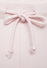 Ljust rosa sweatpants har en texturerad tygkvalitet, elastisk midja och en flätad dragsko som är knuten i en rosett med fransiga ändar.