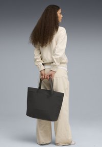 Sac fourre-tout noir avec des poignées robustes et un design minimaliste. Fabriqué en matériau lisse, il présente une forme simple et épurée sans embellissements.
