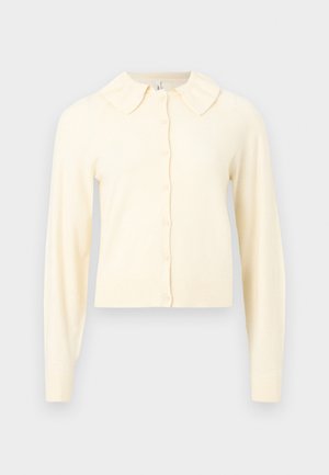 Κρεμ-χρωματιστή μακριά ζακέτα με κουμπιά στο μπροστινό μέρος και μικρό, στρογγυλεμένο γιακά, σε απλό φόντο.