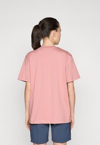 T-shirt de algodão rosa com um corte descontraído, mangas curtas e decote redondo. A parte de trás é lisa com um design simples. Combinado com calções azul-escuro.