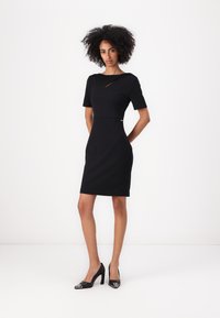 Must vald Kleid lühivarrukatega, diskreetne lõige kaeluses, sile tekstuur. Kombineeritud mustade kõrgete kontsadega, millel on metallilised detailid.