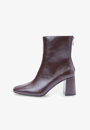 Botte de cheville en cuir marron avec un bout pointu et un talon épais. Texture brillante, fermeture éclair sur le côté et design élégant.