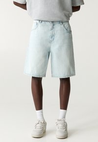 Shorts di denim azzurro chiaro con una vestibilità ampia, design classico a cinque tasche e orlo sfrangiato, abbinati a calze bianche e sneaker.