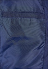 Tessuto blu navy con una superficie liscia e cuciture visibili, dotato di una tasca orizzontale sul lato sinistro.