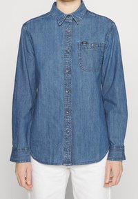 Blå denimskjorta med långa ärmar, knapp-down krage, bröstficka och logotypapplikation. Har en lätt blekt textur och rundad fåll.