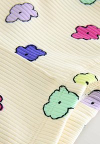 Gros plan sur un tissu côtelé avec des motifs colorés en forme de nuages violet, rose, vert, jaune et lilas sur fond crème.