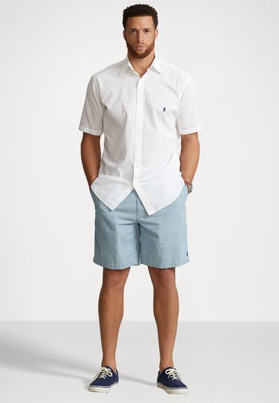 Hvid kortærmet skjorte med knapper, lys blå shorts og marineblå sneakers. Skjorten har et lille logo; shortsene er ensfarvede med en afslappet pasform.