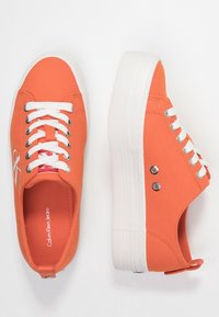 Orange canvas sneakers med vita snören, rund tå och platå-sula. Har Calvin Klein Jeans-logotyp på sidan och silverfärgade ögla.