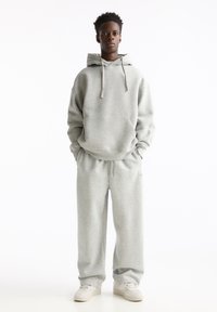 Grauer Sweatshirt mit Kapuze, frontaler Tasche und Kordeln, kombiniert mit passenden grauen Sweatpants. Glatte Textur, lockere Passform, minimale Markenkennzeichnung.